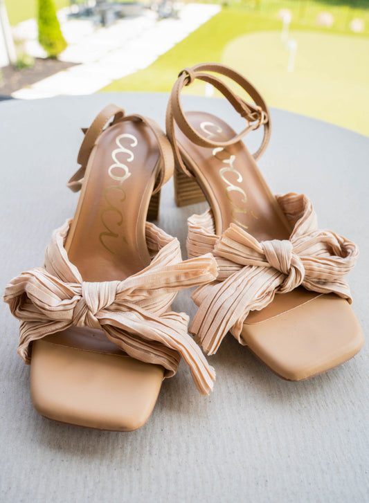 A strappy square toe, bowed heel. The bowls made up of a textured cloth that criss crosses. An ankle strap for extra security and a chunky heel for ease. The heel is a medium beige and the bow is a light beige.