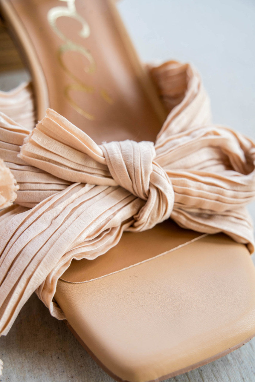 A strappy square toe, bowed heel.  The bowls made up of a textured cloth that criss crosses.  An ankle strap for extra security and a chunky heel for ease. The heel is a medium beige and the bow is a light beige.