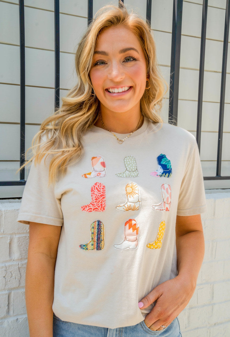 Beige, high scoop neck tee-shirt. This soft tee has 9 hand-stitched cowboy boots in a grid of 3x3.  Each cowboy boot is made of a different fabric. Model is wearing a size medium.