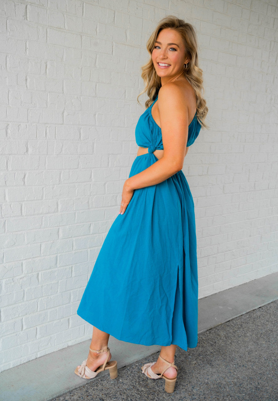 This one shoulder cut out dress has a capped sleeve that cuts on a diagonal with a midriff cutout on the opposite side. The pieces are connected in a scrunched tie for a unique beachy look.  This dress comes in a beautiful turquoise color. It is s super light weight and runs true to size. The model is 5’9” and wearing a medium and the dress falls at a 3/4 length below the calf.