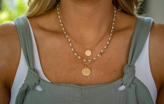 3 layered gold necklace. The first and third layer are gold chains with a flat gold coin pendant, the first layer’s pendant is smaller than the third layer. The second layer is a white and gold alternating beading.