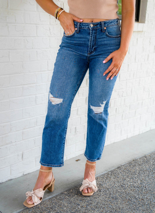 High Rise Slim straight-leg denim jeans featuring a medium to dark wash.  Just slightly frayed at the knees for a worn look. These jeans have two front and two back pockets. They run true to size and have stretch. The model is 5’9” and wearing a size 28.